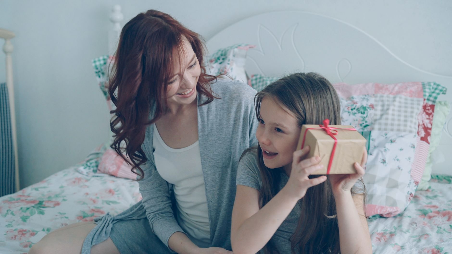 Mother and daughter sharing a joyful moment while opening a gift box on a cozy bed